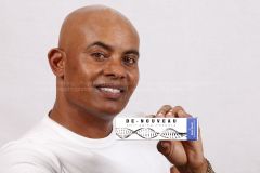 A man with a shaved head and a white shirt smiles while holding a blue and white box labeled "De-Nouveau Anti-Aging Formula." The background is plain white, and the box features a DNA double helix design. Text with email addresses is slightly visible but faded across the middle of the image. pictures images stock photography getty shutterstock