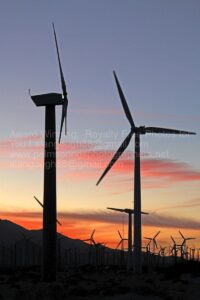 alternative, energy, wind, turbines, jean, manning. nassim, haramein Wind turbines in motion silhouetted against a vibrant sunset sky with hues of orange, pink, and purple. The landscape shows mountain outlines in the background. Text on the image reads: "Award Winning, Royalty Free Photos," along with contact information. pictures images stock photography getty shutterstock